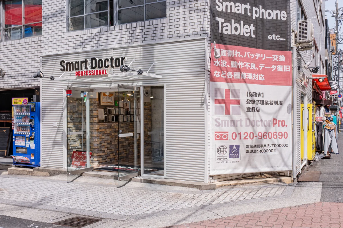 スマートドクタープロ心斎橋 外観側面——総務省登録修理業者制度登録店（電気通信事業法：T000002・電波法：R000002）・ISO9001:2015認証・intertek・UKAS認定を外壁に掲示