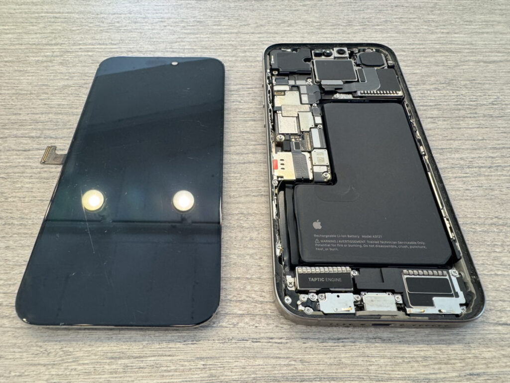 iPhone 15 Proを分解し、取り外したフロントパネルと内部を確認している様子。水没の痕跡を確認して内部洗浄を実施