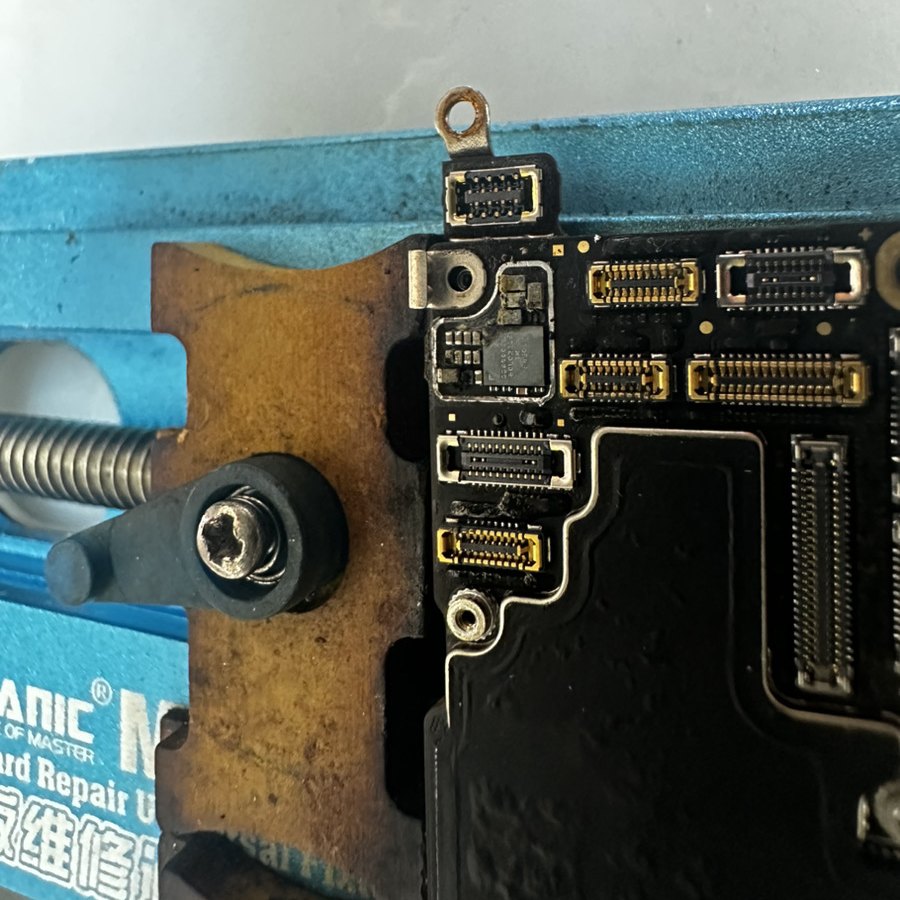 治具に固定したiPhone 14 Proの基板の拡大。コネクタ脇のIC周辺に水没による白い残留物と腐食が見える