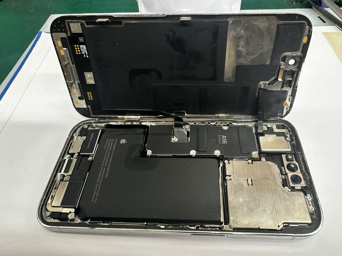 分解したiPhone 14 Pro。ディスプレイを開いた内部にバッテリーとA16 Bionic搭載のロジックボードが見え、フレームに水没の痕が残っている